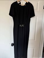 Black short-sleeved dress hanging on a hanger with a door in the background.
