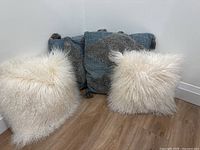 Four throw pillows arranged against corner wall: two white fluffy pillows and two blue textured pillows