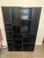 Front view of the large solid black wood shelf unit showing multiple compartments of various sizes.