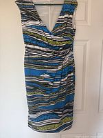 Sleeveless wrap dress with V-neckline and colorful horizontal stripes in blue, green, black, and white hung on door