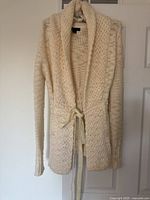 Front view of a large cream knit women's sweater showing knit pattern and belt tie at waist.