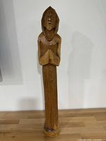 Front view of a hand-carved wood statue showing a hooded figure with praying hands.