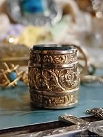 Barrel-shaped fob charm upright showing detailed floral engraving around circumference