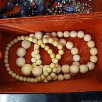 Top view of bone bead necklace coiled inside red fabric-lined box alongside other necklaces