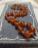 Necklace laid out showing smooth round orange carnelian beads separated by smaller transparent rock crystal spacers on a decorative fabric background.