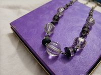 Close-up showing faceted round clear crystal beads alternating with small black onyx beads on light purple background.