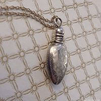 Close-up photo of an antique sterling silver bottle-shaped pendant necklace, showing the etched decorative pattern on the bottle pendant and part of the chain.