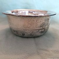 Side view of the antique sterling silver bowl showing engraved text and decorative border with tarnish and wear.