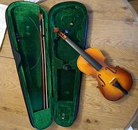 Open hard case with green velvet interior holding the bow and violin alongside it on a wooden surface.