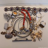 Assorted jewelry pieces including bracelets, brooches, rings, pins, and tie bar. Some items have gemstones, beads, and ornate detailing. Several pieces appear worn and require cleaning.