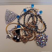 Photo of mixed jewelry items showing rhinestone brooch, blue bead necklace, gold chains, earrings and charms.