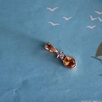 Gold pendant with an oval yellow gemstone and a clear star-shaped gemstone on a blue background.