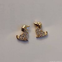 Front view of tiny dog-shaped gold-plated earrings encrusted with clear cubic zirconia stones on the body, showing detailed design and shape.