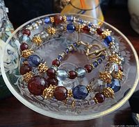 Photo showing the vintage carnelian necklace coiled in a small etched glass bowl highlighting the different beads and gold-toned spacer elements.