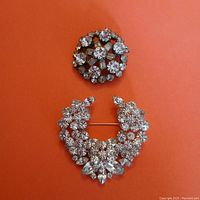 Front view of the round and crescent-shaped rhinestone brooches on orange background