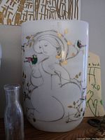 Front view of white porcelain vase showing female figure with colorful birds and gold leaf details