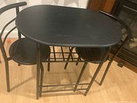 Photo of black oval bistro table with two matching chairs tucked underneath, showing design and condition.