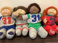 Front view showing four Cabbage Patch dolls with different outfits and hair colors, seated upright