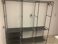 Front view of black metal rack with multiple shelves and hanging hooks assembled against a wall.