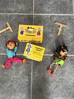Two vintage Pelham marionette puppets with wooden control bars and original boxes on tiled floor.