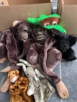 Full view of six hand puppets inside cardboard box showing multiple animal characters including gorillas, frog, monkey, rabbit and partially visible black puppet.