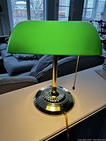 Front view of green glass shade bankers lamp on white surface with visible tarnish on brass base.