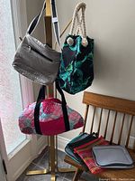Photo of three tote bags: Bench gray quilted shoulder tote, black tote with green leaf pattern and rope handles, pink floral duffel bag hanging from lamp post, with fabric organizers on chair beneath.