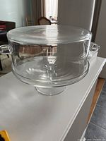 Side view of the glass cake platter with the dome lid covering it, showing the overall shape and size, lid with handles, and small chip in rim.