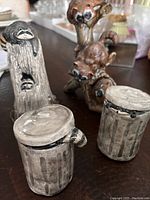 Four ceramic raccoon-themed pieces on a wooden surface showing two figurines and two small containers