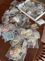 Multiple plastic bags containing assorted necklaces, bracelets and earrings spread on wooden table