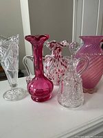 Five glass vases and decanters including cranberry glass and clear cut glass on a white surface