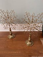 Two gold metal snowflake decorations standing on wooden floor against wall.