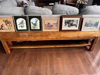 Wide shot showing all six framed pictures on wooden bench including wildlife, birds, horses, and landscapes.