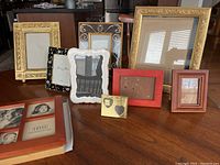Photo showing 10 assorted picture frames arranged on table in various styles and sizes including ornate gold frames, red and brown wood frames, ceramic and metal frames.