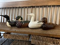 Side view of four duck decoys on wooden bench showing wooden painted and white porcelain decoys.