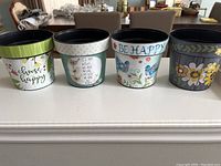 All five decorative plastic pots lined up showing different cheerful designs and messages, placed on table.