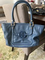 Front view of blue leather Tory Burch purse, showing flap with logo and handles.