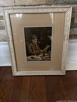 Frontal photo of the vintage framed print showing the man reading a newspaper and the distressed ornate beige frame.