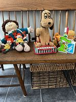 Wide shot showing all toys in lot on wooden bench, including Cabbage Patch Kids doll, Disney Pluto plush on tin, Pippi dolls, and other vintage toys.