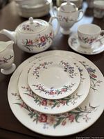 Stack of dinner plate, dessert plate, saucer with teapot, creamer, sugar bowl and teacup in background showing floral pattern