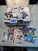 Top view of multiple stacks of hockey cards inside a vintage suitcase, with several cards spread out in front showing players in various team uniforms, some with holographic effects.