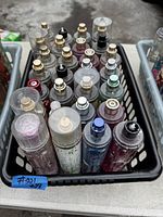 Top down view of 28 assorted bath and body spray bottles in a black basket.