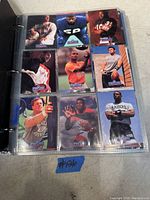 Football trading cards in plastic sleeves inside a binder, visible nine cards on one page including players in varied team uniforms.