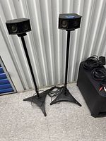 Two black tall Bose speakers on black metal stands with cables visible on floor.