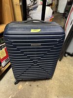 Photo showing the front of the Bugatti dark blue hard shell suitcase with 4 wheels and a handle, placed upright on the floor.