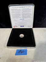 Full view of the open silver metal presentation case with a black velvet interior holding the Canadian 25 cent coin and an informational insert in the lid about the Millennium series.