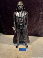 Front view of Darth Vader action figure standing on a white surface with a dark backdrop. Figure is in good condition with painted details.
