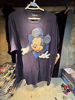 Navy blue Disney T-shirt with large Mickey Mouse graphic on front, hung on white plastic hanger.
