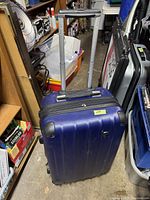 Front view of blue Heys suitcase showing telescopic handle extended, four wheels, and hard shell surface.