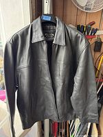 Front view of black leather men's winter coat hanging on a hanger showing the smooth leather exterior and classic collar.